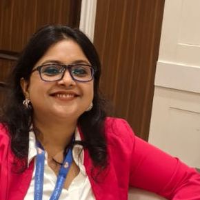 Sabiya Khan smiling in glasses and a pink blazer over a white blouse, photographed from the chest up